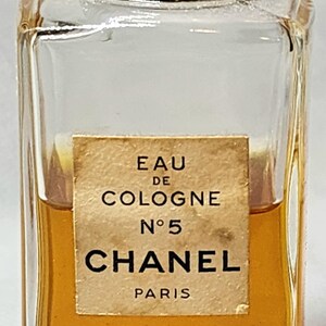 May include: A vintage Chanel No. 5 Eau de Cologne bottle. The clear glass bottle contains a golden liquid and has a black cap. The label reads "Eau de Cologne No. 5 Chanel Paris."