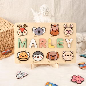 Könnte beinhalten: Holz-Namenspuzzle mit dem Namen "MARLEY" in bunten Buchstaben. Das Puzzle enthält Tierformen wie Hirsch, Koala, Pferd, Kaninchen, Biene, Pinguin, Hund und Katze. Das Puzzle ist aus hellem Holz gefertigt und für Kinder konzipiert.