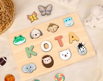 May include: A wooden puzzle board with the name "KOTA" spelled out in colorful letters. The board features various animal and insect cutouts, including a frog, a dog, a monkey, a zebra, a hedgehog, an elephant, and a butterfly.