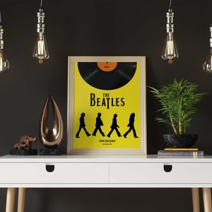 Puede incluir: Un escritorio blanco con dos cajones y un p&oacute;ster enmarcado de The Beatles con el texto "The Beatles Come Together" sobre un fondo amarillo. El p&oacute;ster presenta una silueta negra de los miembros de la banda caminando por una calle. Hay tres bombillas colgantes sobre el escritorio.