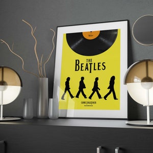 Puede incluir: Un p&oacute;ster enmarcado en negro con fondo amarillo que presenta un disco de vinilo negro y el texto "The Beatles" y "Come Together". El p&oacute;ster se exhibe en un estante con dos l&aacute;mparas de globo marr&oacute;n y blanco y un jarr&oacute;n con ramas secas.