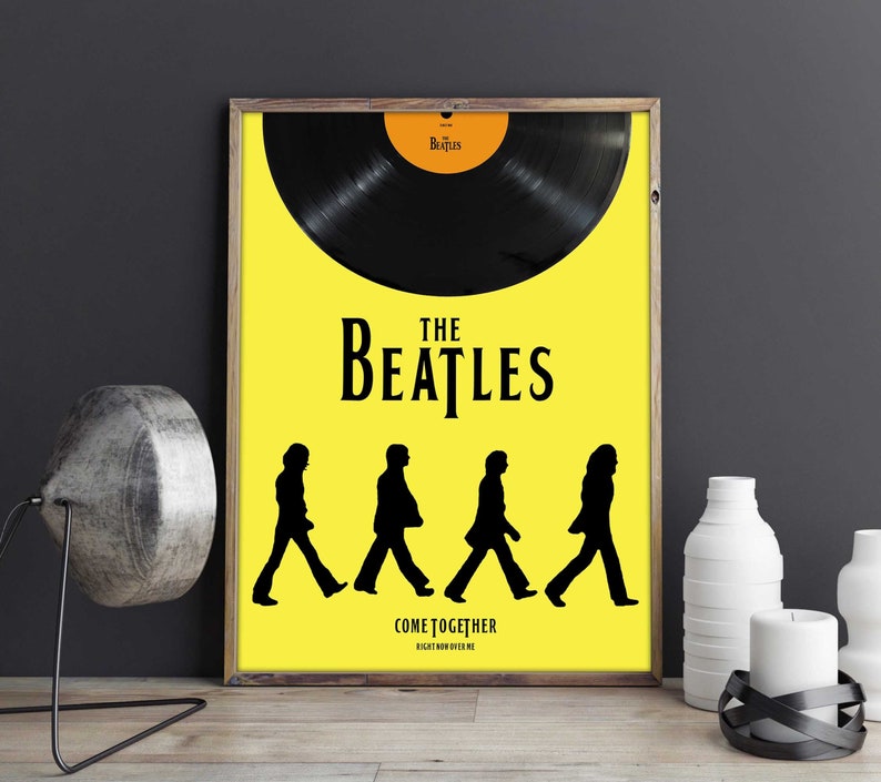 Puede incluir: Un p&oacute;ster amarillo con una silueta de disco de vinilo negro y el texto "The Beatles" en negro. Debajo del texto hay cuatro siluetas negras de los Beatles caminando en fila. El texto "Come Together" est&aacute; debajo de las siluetas, con las palabras "Right Now Over Me" en una fuente m&aacute;s peque&ntilde;a debajo.