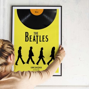 Puede incluir: Un p&oacute;ster enmarcado en negro con fondo amarillo que presenta un disco de vinilo negro, el texto "The Beatles" y una silueta de los miembros de la banda caminando por un paso de cebra. El texto "Come Together" est&aacute; debajo de las siluetas.