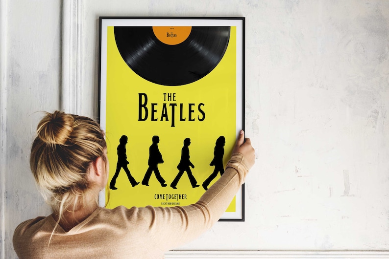 Puede incluir: Un p&oacute;ster enmarcado en negro con fondo amarillo que presenta un disco de vinilo negro, el texto "The Beatles" y una silueta de los miembros de la banda caminando por un paso de cebra. El texto "Come Together" est&aacute; debajo de las siluetas.