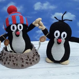 May include: Two crocheted mole plushies. One mole is wearing a red and blue striped hat and holding a brown stick. The other mole is holding a pink flower.