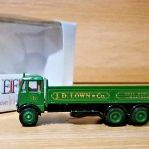 May include: A green die-cast model lorry with black wheels and chassis. The side of the lorry bed features gold lettering that reads J.D. TOWN & Co. COAL MERCHANTS MARTHAM 341. The cab has a small circular logo and the lorry is positioned near its box.