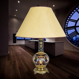 May include: A table lamp with a cream-coloured lampshade and a decorative ceramic base with gold accents and colourful floral designs.
