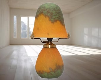 May include: A table lamp with a green and orange glass shade. The shade has a mottled pattern and is mounted on a brass base.