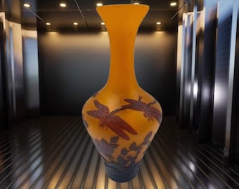 May include: A tall, amber-coloured glass vase with an etched design of dragonflies and floral motifs. The vase has a narrow neck and a wide, rounded base.