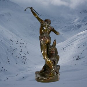 May include: Bronze sculpture of a nude figure holding a bow and arrow, standing on a wolf. The sculpture is set against a snowy mountain backdrop.