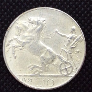 May include: Silver Italian coin with a depiction of a chariot pulled by two horses. The coin has the year 1931 and the denomination L.10.