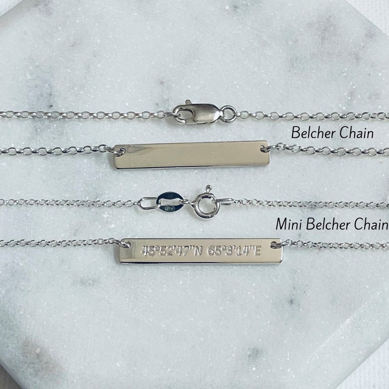 Puede incluir: Dos collares plateados con colgantes de barra y cadenas finas. El collar superior est&aacute; etiquetado como "Belcher Chain". El collar inferior, etiquetado como "Mini Belcher Chain", tiene coordenadas grabadas. Ambos collares tienen cierres.