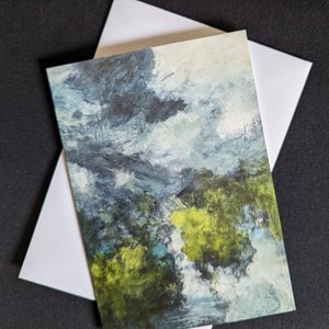 Op de afbeelding: Een wenskaart met een abstract landschapsschilderij in blauw, groen en wit. De kaart wordt geleverd met een witte envelop, tegen een zwarte achtergrond.