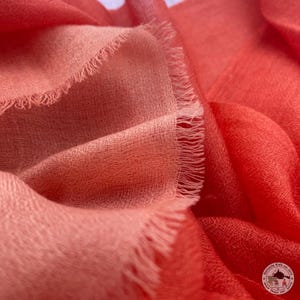 Peut inclure: Gros plan sur une écharpe douce et ombrée dans des tons de rose et de rouge. L'écharpe a un bord effiloché et une texture tissée délicate.