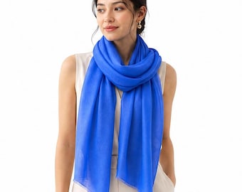 May include: A vibrant royal blue scarf with a lightweight, semi-sheer texture and delicate fringed edges, draped loosely around the neck over a sleeveless cream-colored top. The fabric displays a smooth, consistent weave and a bright, solid color.