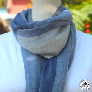 May include: A blue and gray scarf draped around a mannequin's neck. The scarf has a striped pattern with varying shades of blue and gray. The scarf is made of a soft, lightweight material, perfect for adding a touch of color and warmth.