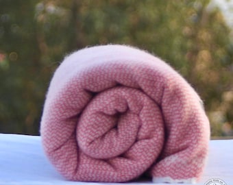 May include: A pink and white woven blanket rolled up. The blanket is made of a soft, fuzzy material.