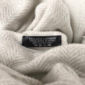 May include: A black label with white text that reads "Exclusive Cashmere Hand Made in Nepal Dry Clean Only". The label has a care tag with symbols for dry clean only, no bleach, no tumble dry, and low iron.