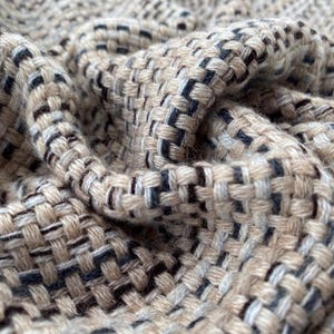 Puede incluir: Primer plano de una tela tejida con un patrón texturizado. La tela es una mezcla de hilos beige, marrón y negro.