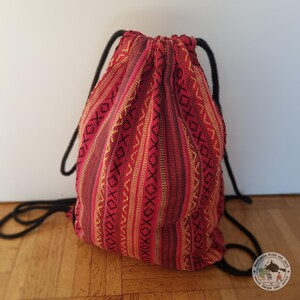 Könnte beinhalten: Rote und gelbe Kordeltasche mit geometrischem Muster. Die Tasche ist aus gewebtem Stoff und hat einen schwarzen Kordelzug.