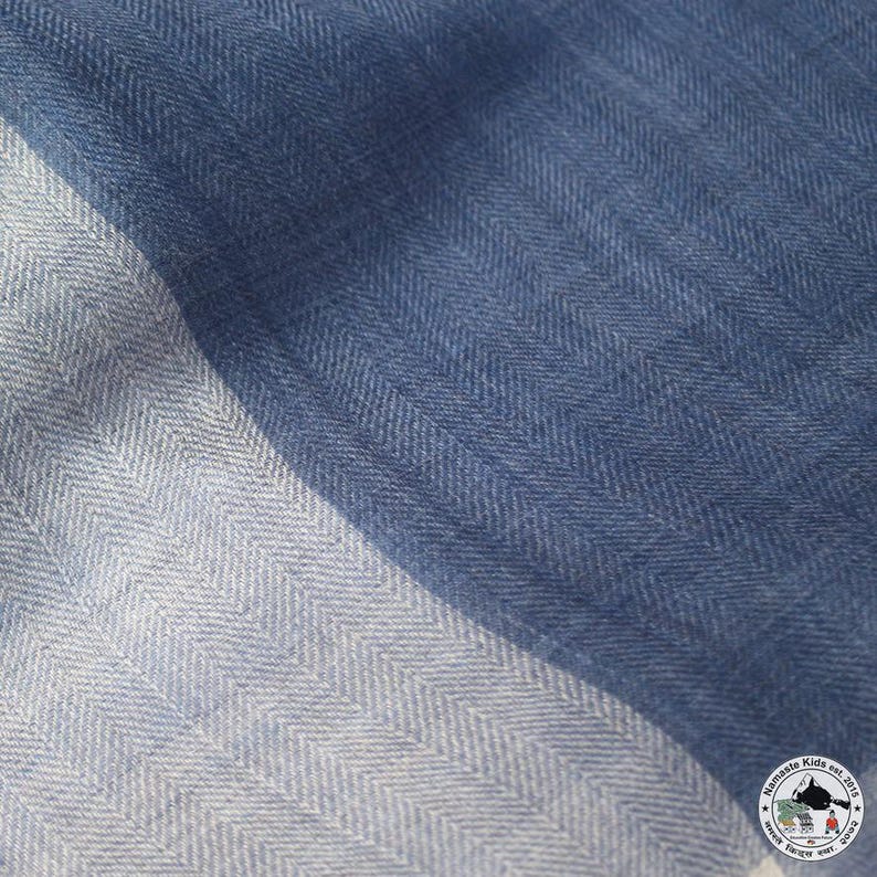 May include: Close-up of a blue and white striped scarf with a herringbone pattern. The scarf has a diagonal design with a light blue and white stripe on the left and a darker blue on the right. The scarf is made of a soft, woven fabric.