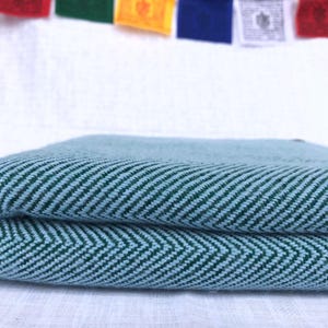 Könnte beinhalten: Eine gefaltete blaue und grüne gestreifte Wolldecke mit Fischgrätenmuster.