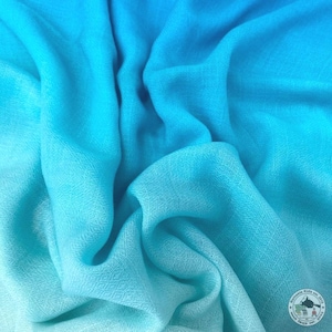 May include: A close-up of a soft, flowing fabric in shades of blue, transitioning from a deep turquoise to a lighter, almost white hue. The fabric has a subtle woven texture, creating a gentle, rippling effect. The overall theme is a textile.