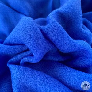 Könnte beinhalten: Nahaufnahme eines weichen, blauen Stoffes mit einer strukturierten Webart. Der Stoff ist gefaltet und drapiert und zeigt seine glatte und luxuriöse Haptik.