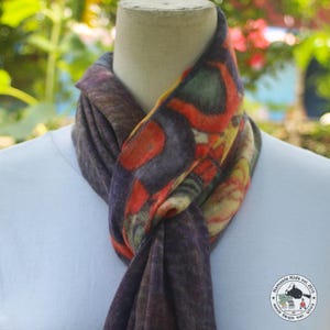 Könnte beinhalten: Ein farbenfroher Schal mit einem Muster aus roten, orangen, gelben und grünen Formen auf dunklem lila Hintergrund. Der Schal ist um den Hals einer Schaufensterpuppe drapiert und zeigt sein Design und seine Textur. Der Schal besteht aus einem weichen Material.