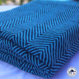 Könnte beinhalten: Gefaltete Decke mit blauem und schwarzem Zickzackmuster. Das Design der Decke weist ein sich wiederholendes Zickzackmuster in Blau- und Schwarztönen auf. Der Stoff wirkt weich und einladend, um Wärme und Stil zu verleihen.