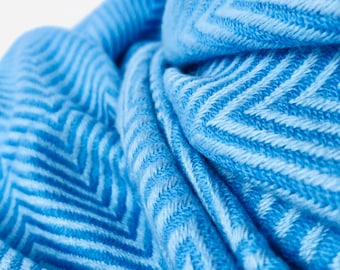 Puede incluir: Primer plano de una bufanda azul suave con un patrón de chevrón repetido. La bufanda está hecha de un material tejido y está doblada, creando una apariencia texturizada y en capas. El color es un azul brillante y vibrante.