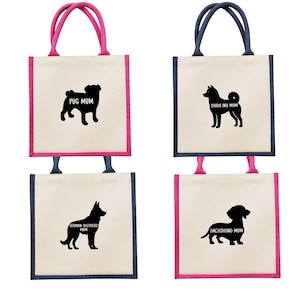 Könnte beinhalten: Vier Tragetaschen mit verschiedenen Hunderassen und dem Text "[Rasse] MUM" auf jeder Tasche. Die Taschen sind aus natürlicher Leinwand mit rosa und blauem Besatz.