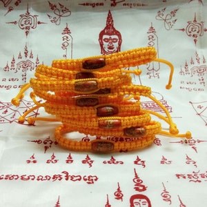 May include: A stack of yellow braided bracelets with red and orange beads. The bracelets are on a white background with red writing.