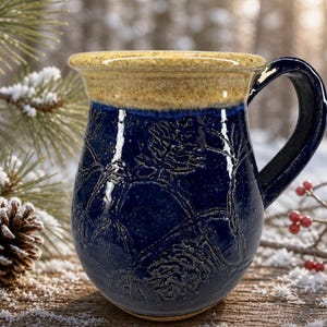 May include: A handcrafted ceramic mug with a dark blue glaze and a textured botanical design. The rim is a light tan color, and the handle is dark blue. This mug is perfect for enjoying hot beverages.