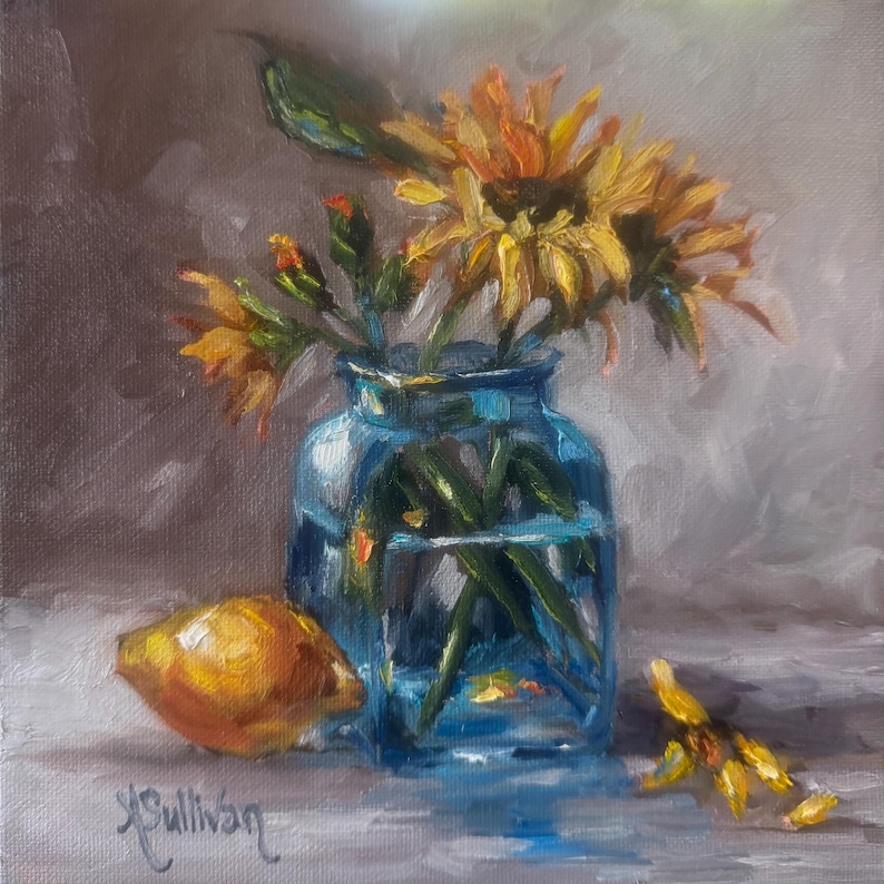 May include: An oil painting of a still life featuring yellow sunflowers in a blue glass vase, a lemon, and fallen petals. The artwork is signed "K. Sullivan" in the lower left corner. The background is a soft gray.