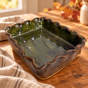 May include: A rectangular ceramic baking dish with a glossy, deep green glaze and a dark brown exterior. The dish features a distinctively wavy, scalloped rim and a smooth, reflective interior surface, showcasing a handcrafted, organic aesthetic.
