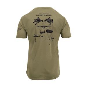 May include: Olive green t-shirt with a graphic on the back featuring the text "US ARMY PATHFINDER PUPPET MASTER". The graphic includes illustrations of helicopters, parachutes, and the phrase "FIRST IN LAST OUT".