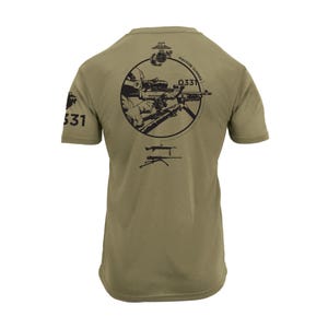 May include: Olive green t-shirt featuring a black graphic on the back. The graphic includes a circular design with a soldier aiming a machine gun, the text "MACHINE GUNNER", and the number "0331". The left sleeve displays the number "531".