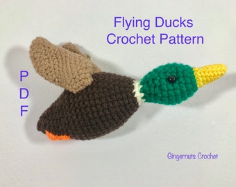 May include: Crochet pattern for a flying duck. The duck is brown, green, and yellow. The pattern is available as a PDF download. The text "Flying Ducks Crochet Pattern" is at the top of the image. The text "GingerNuts Crochet" is at the bottom of the image.