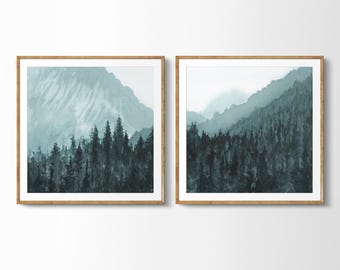 May include: A set of two framed watercolor prints depicting a misty forest scene with a mountain range in the background. The prints are in shades of blue and green.