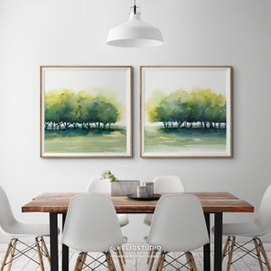 Pode incluir: Duas pinturas em aquarela de uma fileira de &aacute;rvores em tons de verde e azul, sobre um fundo branco. As pinturas s&atilde;o emolduradas em madeira e penduradas em uma parede branca acima de uma mesa de madeira com cadeiras brancas.