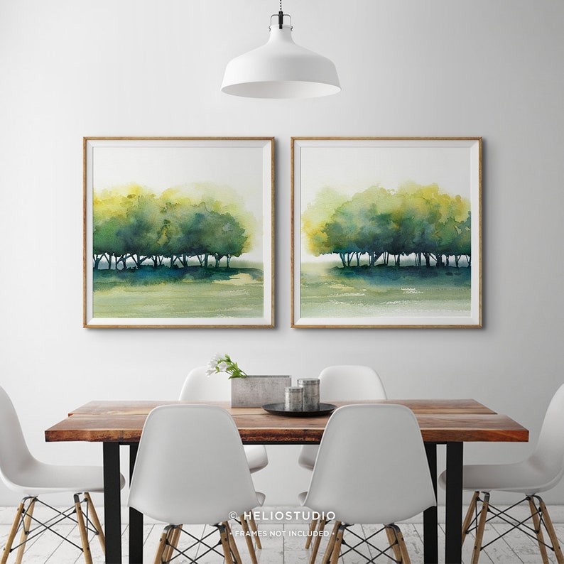 Pode incluir: Duas pinturas em aquarela de uma fileira de &aacute;rvores em tons de verde e azul, sobre um fundo branco. As pinturas s&atilde;o emolduradas em madeira e penduradas em uma parede branca acima de uma mesa de madeira com cadeiras brancas.
