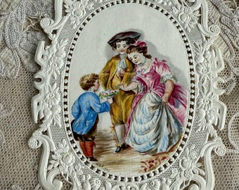 May include: An oval picture, framed in white, depicting a scene of three figures in historical attire. A boy presents flowers to a couple. The frame has an ornate, decorative design, set against a lace backdrop.