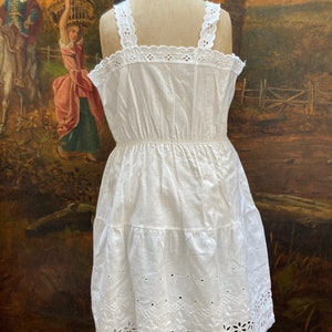 May include: White cotton dress with eyelet lace trim and a tiered skirt. The dress has a fitted bodice and a gathered waist.
