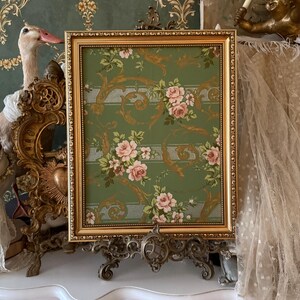 May include: A gold framed picture with a green background and a floral pattern. The picture is on a decorative stand with ornate details.