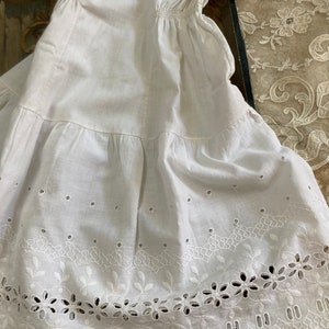 May include: White cotton undergarment with a scalloped lace trim and eyelet embroidery. The garment has a gathered waist and a tiered skirt.