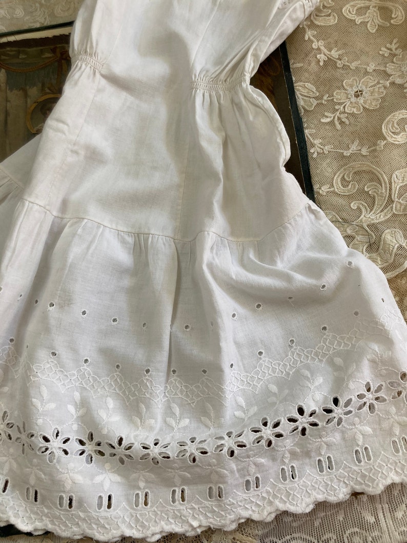 May include: White cotton undergarment with a scalloped lace trim and eyelet embroidery. The garment has a gathered waist and a tiered skirt.