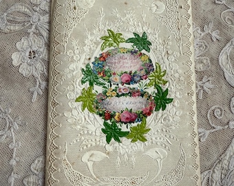 Puede incluir: Una tarjeta de felicitación antigua, de color blanquecino, con intrincados detalles de encaje. La tarjeta presenta un diseño floral central con texto, rodeado por un borde decorativo. La estética general es delicada y vintage.