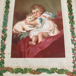 May include: A vintage Christmas card featuring a young girl in a white dress holding a white cat. The card has a green holly border and the text "Amy and Bot." is written in black ink.