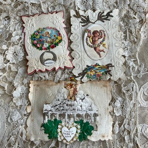 May include: Three vintage Valentine's Day cards with intricate lace designs and cherub imagery. The cards feature embossed details, including a cherub holding a wreath, a cherub in a building, and a cherub with a heart that reads "Fondly Thine in Love".